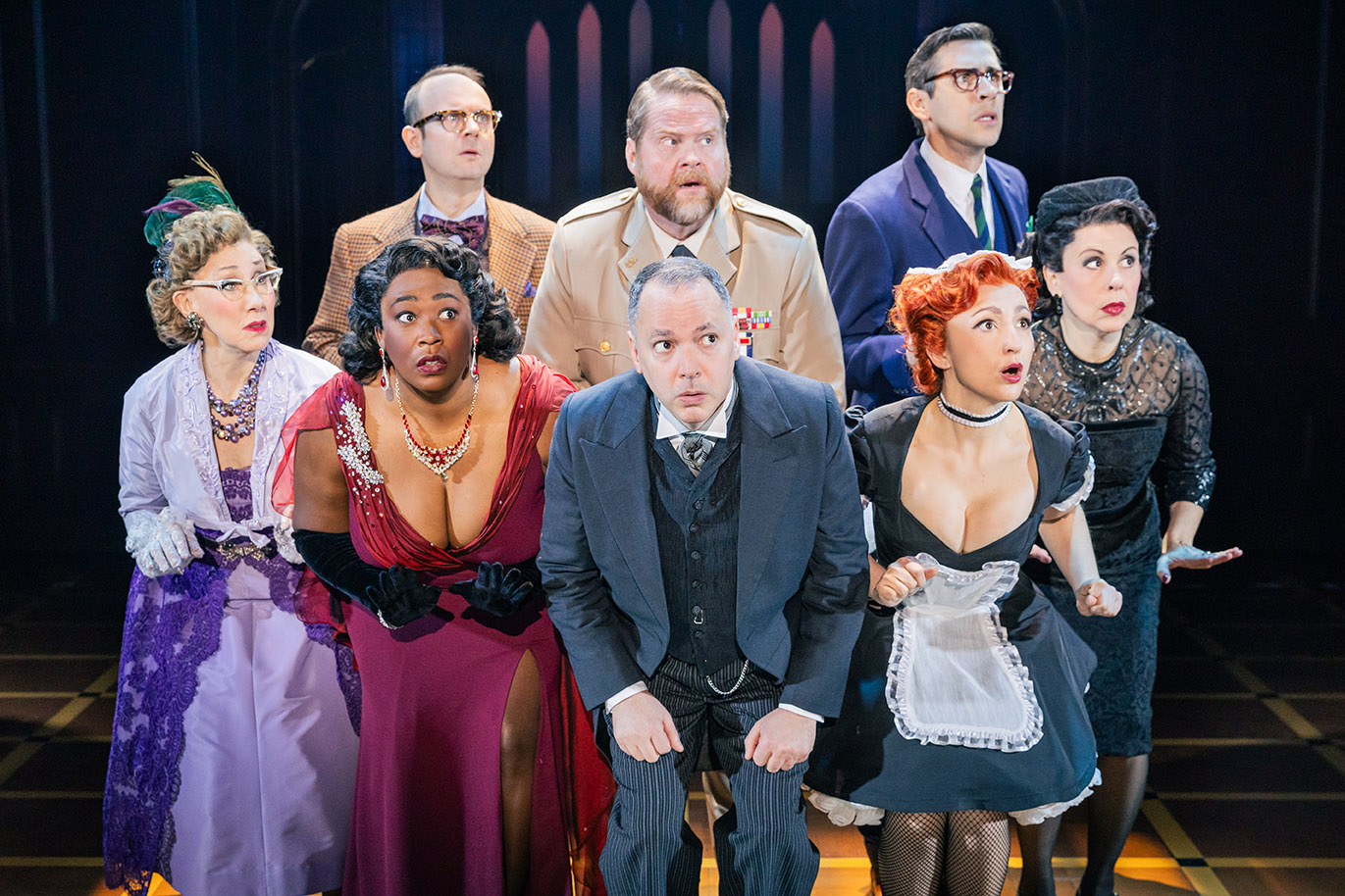 The Company of the North American tour of CLUE - photo by Evan Zimmerman for MurphyMade<br><br>Four women and a man stand on stage crouched in a line with three men standing behind them as they search for something. All actors are looking to their left off in the distance with a frightened look on their faces.